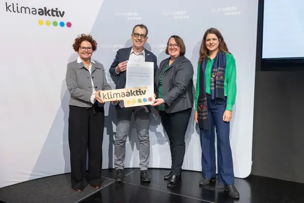 4 Personen mit Urkunde und klimaaktiv Schild schauen in die Kamera