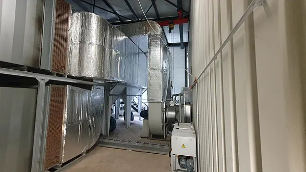 Ein großes Lüftungssystem mit wärmegedämmten Leitungen und Kupfer-Wärmetauschern in einer Industriehalle. Im Vordergrund ist ein elektrisch betriebenes Gerät zu sehen.