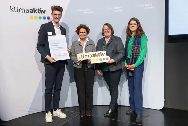 4 Personen mit Urkunde und klimaaktiv Schild schauen in die Kamera