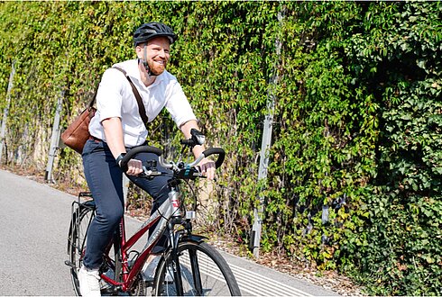 Mann in weißem Hemd und brauner Umhängetasche fährt am Fahrrad in die Arbeit