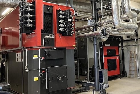 Große rote Heizkessel mit Rohrleitungen und Steuerungselementen in einem Heizraum für Hackschnitzel-Anlagen.