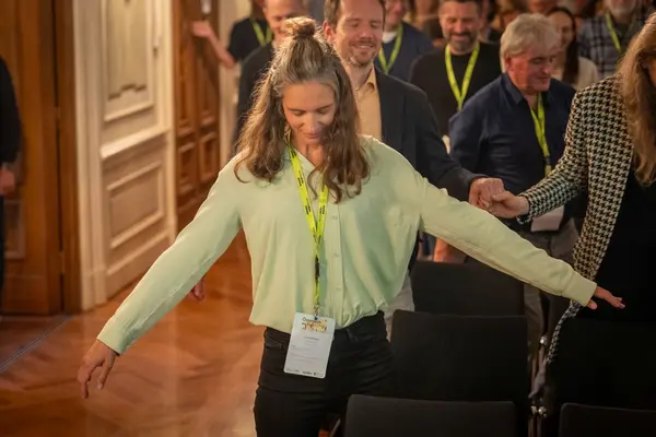 Renate Platzer mit geschlossenen Augen im großen Saal, im Hintergrund weitere Personen mit geschlossenen Augen