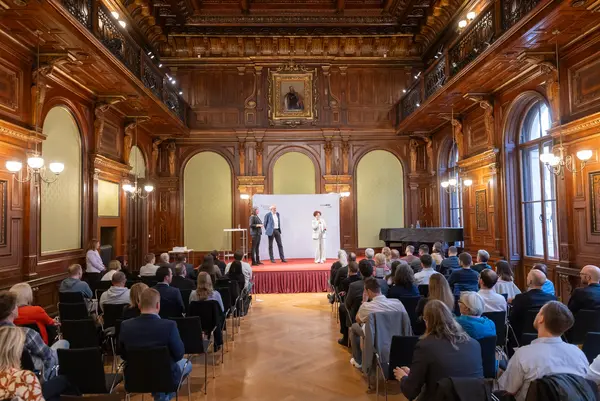 ein Festsaal mit Bühne, Publikum und Menschen auf der Bühne