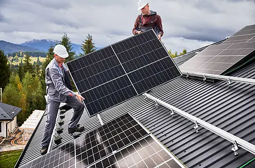 Zwei Installateure befestigen eine Solaranlage am Dach eines Hauses