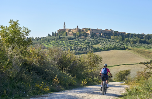 Radfahrer von hinten in der Toskana. In der Ferne hügelige Landschaft und ein Dorf am Hügel