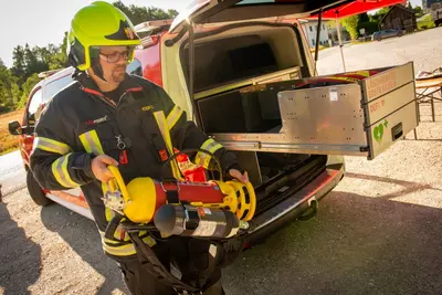 hinten offenes E-Kommandofahrzeug, davor ein Feuerwehrmann in voller Montur