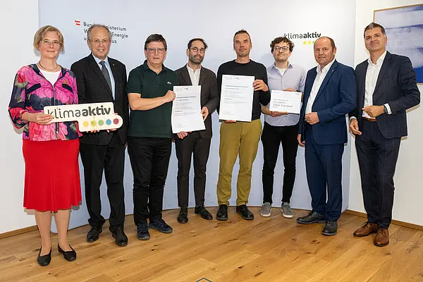 eine Gruppe von Menschen auf einer Bühne hält Urkunden in die Kamera