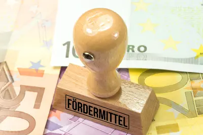 Ein Holzstempel mit der Aufschrift „Fördermittel“ liegt auf mehreren Euro-Geldscheinen.