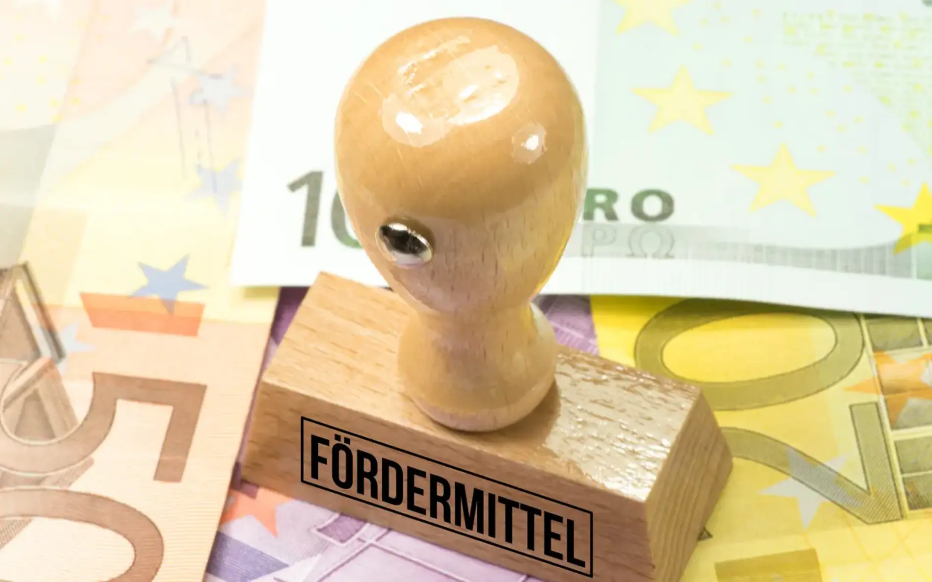 Ein Holzstempel mit der Aufschrift „Fördermittel“ liegt auf mehreren Euro-Geldscheinen.