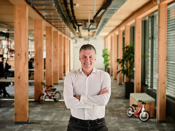 Bernd Hake, CEO von Woom posiert mit verschränkten Armen in einem Gebäude mit Holzsäulen.