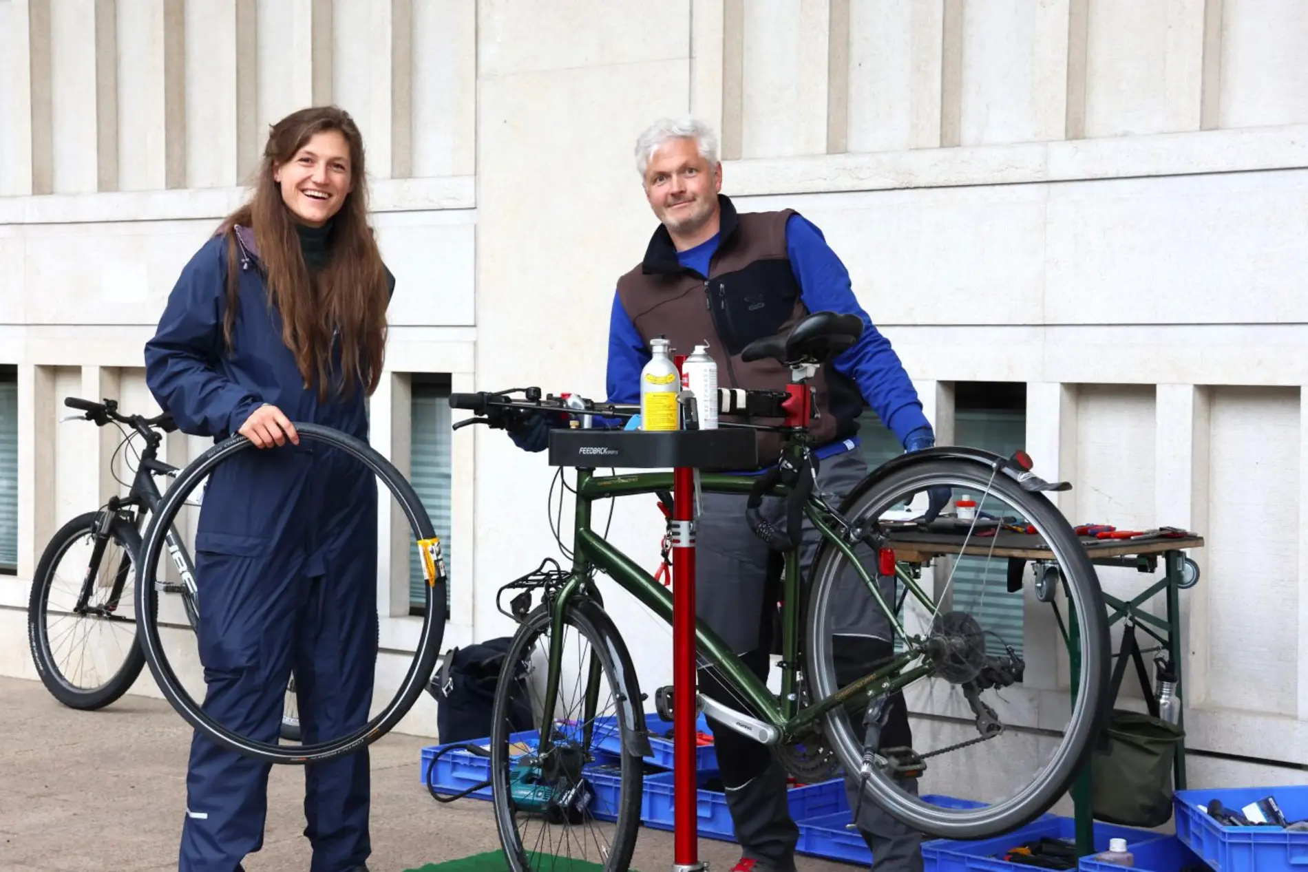 Eine Frau und ein Mann schauen in Kamera, halten Fahrradschlauch und reparieren Fahrrad