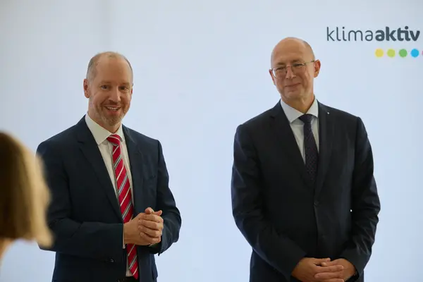 2 Männer in Anzug stehen vor einer Logowand klimaaktiv