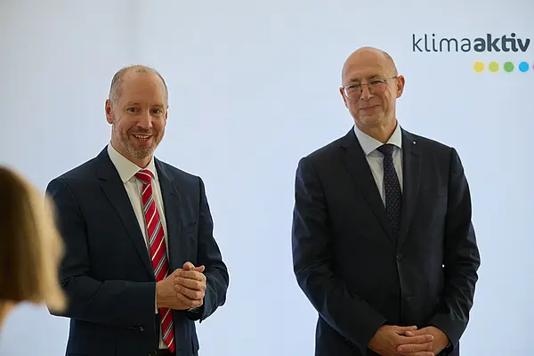 2 Männer in Anzug stehen vor einer Logowand klimaaktiv