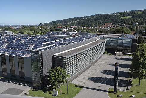 Modernes Büro- und Produktionsgebäude mit großflächigen Photovoltaikmodulen auf dem Dach, umgeben von Straßen und Grünflächen.