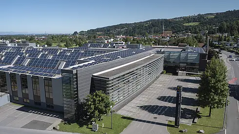 Modernes Büro- und Produktionsgebäude mit großflächigen Photovoltaikmodulen auf dem Dach, umgeben von Straßen und Grünflächen.