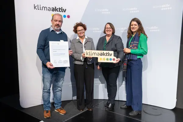 4 Personen mit Urkunde und klimaaktiv Schild schauen in die Kamera