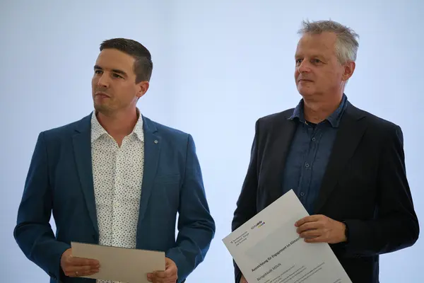 2 Personen mit Urkunden in der Hand schauen nach links